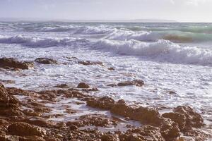sterk golven, spatten en schuim crashen en spatten Aan rotsen Aan een zonnig dag. idyllisch zeegezicht concept. natuur, omgeving, ecologie thema's. ruw zee Aan kust mega's limnionas, chios, Griekenland. foto