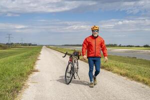 atletisch senior fietser met een grind toeren fiets Aan een dijk spoor langs keten van rotsen kanaal in de buurt graniet stad in Illinois foto