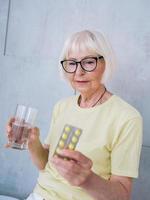senior vrouw in glazen met medicijnen en glas water. leeftijd, gezondheidszorg, behandelingsconcept foto