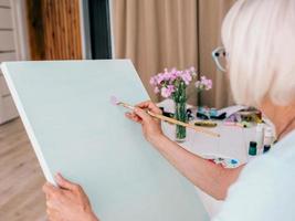 senior vrolijke vrouw in glazen met grijs haar tekenen met potlood bloemen in vaas. creativiteit, kunst, hobby, bezettingsconcept foto
