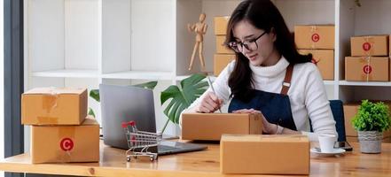 jonge startende eigenaar van een klein bedrijf schrijft adres op kartonnen doos op de werkplek. kleine ondernemer mkb, werken met doos thuis, online verkoop, e-commerce, verpakkingsconcept foto