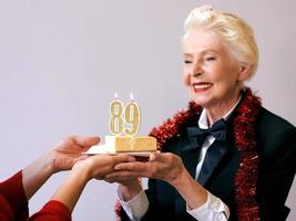 gelukkige vrolijke stijlvolle negenentachtig jaar oude vrouw in zwart pak viert haar verjaardag met taart. levensstijl, positief, mode, stijlconcept foto