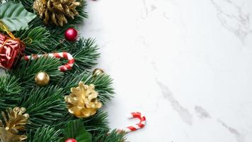 groene dennenboombladeren, rode kerstversieringen en zuurstokken op witte marmeren achtergrond, kerstversiering in felrode kleur. eenvoudig en creatief kerstconcept. foto