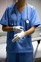 verpleegster in lichtblauw uniform die steriele handschoenen aandoet en een stethoscoop vasthoudt. foto