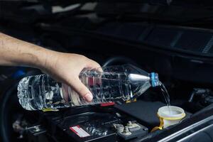 de monteur vult de auto's voorruit wisser tank met water en inspecteert de motor voordat beginnend de reis. auto onderhoud of inspectie concept foto