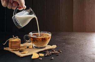 melk room gegoten in koffie beker, latte, cappuccino Aan houten tafel zwart achtergrond en donker kleuren foto