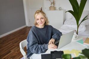 portret van jong blond vrouw met laptop, opname Aan digitaal camera, gemaakt blog, vloggen in haar kamer, bewerken Aan computer foto