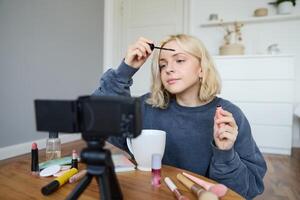 portret van blond glimlachen vrouw records een levensstijl blog, vlogger of bedenken artiest opname voor sociaal media, Holding mascara, herzien schoonheid producten voor volgers online foto