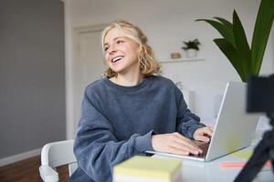 portret van jong blond vrouw, vrouw college leerling werken van huis Aan opdracht, toepassingen laptop, studies van een afstand, zit in kamer in voorkant van computer foto