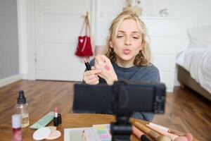 portret van jong vrouw blogger, schoonheid bedenken vlogger, tonen lippenstift stalen Aan haar hand, aanbevelen schoonheidsmiddelen naar haar volgers, creëren inhoud voor sociaal media account Aan digitaal camera foto