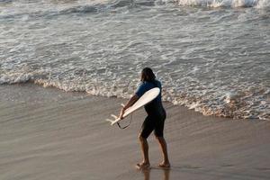 surfer die met zijn board uit de zee komt. gijon strand, asturië, spanje foto