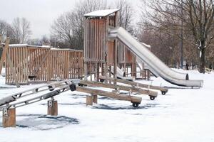 houten speelplaats gemaakt van natuurlijk milieuvriendelijk materiaal in openbaar stad park met sneeuw Bij winter tijd. modern veiligheid kinderen buitenshuis apparatuur. winter activiteiten. kinderen rust uit en spellen Aan Open lucht foto