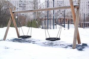 houten speelplaats gemaakt van natuurlijk milieuvriendelijk materiaal in openbaar stad park met sneeuw Bij winter tijd. modern veiligheid kinderen buitenshuis apparatuur. winter activiteiten. kinderen rust uit en spellen Aan Open lucht foto