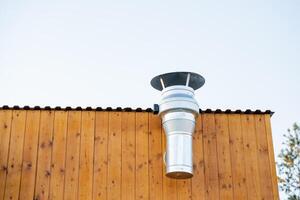 schoorsteen schoorsteen uitgangen de achterzijde van de gebouw, ventilatie door een pijp in de dak, een systeem voor Verwijderen heet lucht naar de straat, een afzuigkap ventilator in een cafe, een houten muur. foto