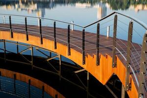 voetganger kruispunt over- de water, houten trap met stappen gemaakt van planken, een weg circulaire omzeilen Aan de meer, een wandelen Oppervlakte Aan de vijver, metaal leuningen van de hek foto