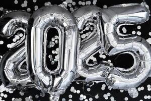 gelukkig nieuw jaar 2025 metalen ballonnen met confetti Aan donker zwart achtergrond. groet kaart zilver folie ballonnen getallen Kerstmis vakantie concept. viering partij felicitatie decoratie foto