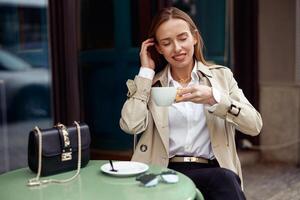 elegant glimlachen vrouw drinken koffie Aan restaurant terras gedurende breken foto