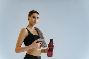 gezond sportief vrouw staand met water fles en telefoon over- studio achtergrond foto