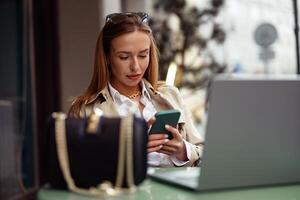 gefocust Europese zakenvrouw gebruik telefoon terwijl werken online zittend Bij buitenshuis cafe terras foto
