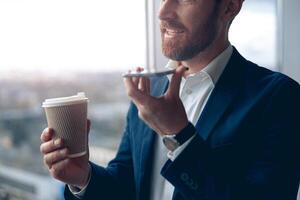 zakenman gebruik makend van smartphone naar Vermelding een stem bericht naar bedrijf partner en drinken koffie foto