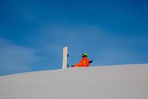 snowboarder freerider met witte snowboard zittend op de top van de skipiste foto