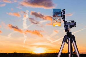 smartphone op statief vastleggen van afbeelding van zonsondergang in verticale modus foto