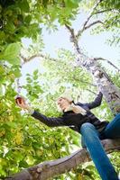 meisje zittend op een appelboom en reikt naar een tak met appels foto