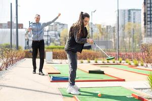 sharing met golf beleven. vrolijk jong Mens onderwijs zijn dochter naar Speel mini golf Bij de dag tijd. concept van vriendelijk familie foto