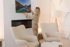 modern huis interieur en huiselijk decor. glimlachen jong vrouw hangende schilderen, zetten foto afbeelding kader Aan de muur. gewoontjes dame nemen zorg van gezelligheid in haar nieuw elegant appartement, profiel