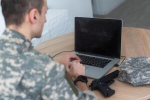 jong spaans Mens leger soldaat gebruik makend van laptop zittend Aan tafel Bij huis foto