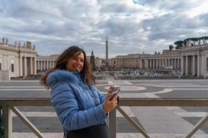 gelukkig midden- oud vrouw toerist gebruik makend van mobiel telefoon in voorkant van san Pietro plein in Rome foto