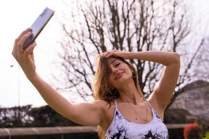 jong charmant blond sportief vrouw in sportkleding poseren nemen een selfie buitenshuis foto