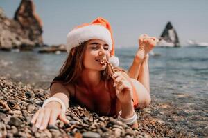 vrouw reizen zee. gelukkig toerist genieten nemen afbeelding Aan de strand voor herinneringen. vrouw reiziger in de kerstman hoed looks Bij camera Aan de zee baai, sharing reizen avontuur reis foto