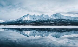 een ver weg visie van met sneeuw bedekt bergen weerspiegeld in de bevroren oppervlakte van een meer foto