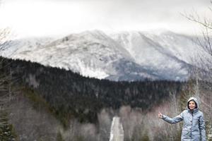 vrouw liftend op een winterweg met prachtige besneeuwde bergen op de achtergrond foto