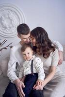 mooi familie zittend Aan sofa met hun weinig jongen in minimalistisch studio foto