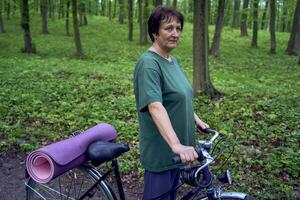 ouderen vrouw wandelen in voorjaar Woud met fiets en yoga mat foto