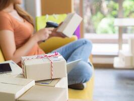 een zakenvrouw is een e-commerce ondernemer zittend Aan een stoel met de Rechtsaf hand- Holding de streepjescode lezer en de links hand- Holding de pakket doos. bedrijf concept. e-commerce concept foto