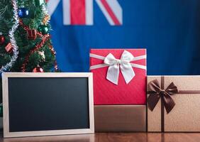 klein schoolbord en geschenk dozen Aan houten tafel met een Kerstmis boom en Australisch vlag in de achtergrond. ruimte voor tekst. concept van Kerstmis en nieuw jaar festival foto