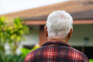 terug visie van een ouderen Aziatisch Mens op zoek Bij zijn huis terwijl staand in een tuin. concept van oud mensen en gezondheidszorg foto