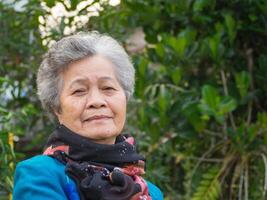 senior vrouw glimlachen en op zoek Bij de camera terwijl staand in een tuin. hoofdschot foto. concept van oud mensen en gezondheidszorg foto