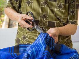 detailopname van senior vrouw handen gebruik makend van een snijdend kleding met schaar foto