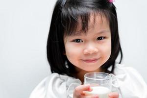 close-up van schattig Aziatisch meisje dat zoet lacht terwijl ze melk drinkt met glas. geïsoleerde witte achtergrond. foto