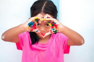 schattig weinig meisje met kleurrijk geschilderd handen Aan muur achtergrond foto