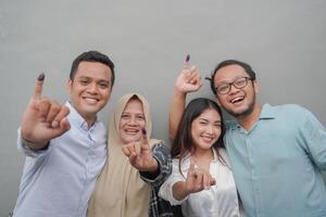 portret van opgewonden Indonesisch familie tonen de weinig vinger gedoopt in Purper inkt na stemmen voor algemeen verkiezing of pemilu voor president en regering, geïsoleerd grijs achtergrond foto