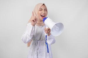 dolblij Aziatisch vrouw vervelend hijab en wit jurk geschreeuw naar de megafoon maken Aankondiging, staand over- geïsoleerd wit achtergrond foto