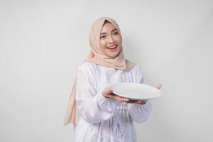 mooi jong Aziatisch moslim vrouw in hijab presenteren een leeg bord met kopiëren ruimte over- het, tonen de voedsel menu voor iftar foto