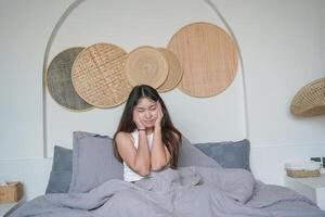 Aziatisch vrouw ontwaken omhoog in de ochtend- gevoel benadrukt en krijgen hoofdpijn na diep slaap, nog steeds gevoel moe en slaperig blijven zittend Aan bed in de slaapkamer foto