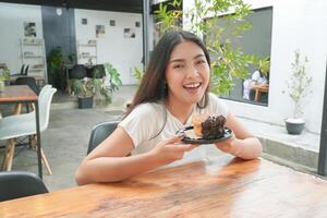 jong Aziatisch vrouw Holding en tonen een zwart bord van donut gebakje genaamd cromboloni met chocola vulling voor tussendoortje tijd, glimlachen met een gelukkig en vrolijk uitdrukking foto