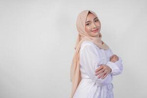 portret van elegant Aziatisch moslim vervelend wit jurk en hijab glimlachen naar de camera met formeel houding Aan wit achtergrond in studio. Ramadhan en schoonheid concept foto